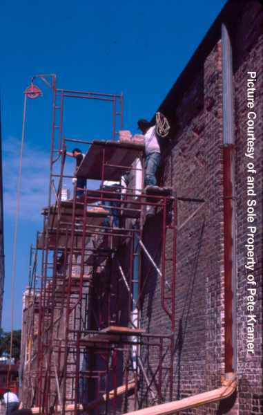 Workers on red scaffolding restoring an old brick building